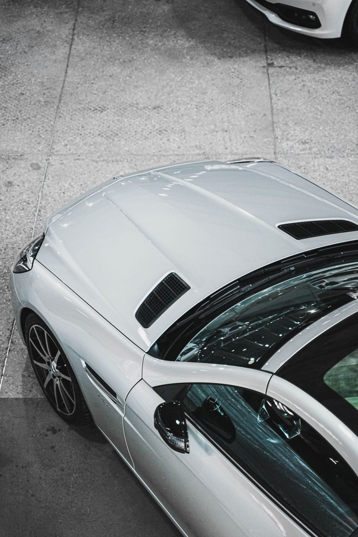 Home Close-up of a sleek silver luxury car in a dealership showroom, showing pristine design and elegance.